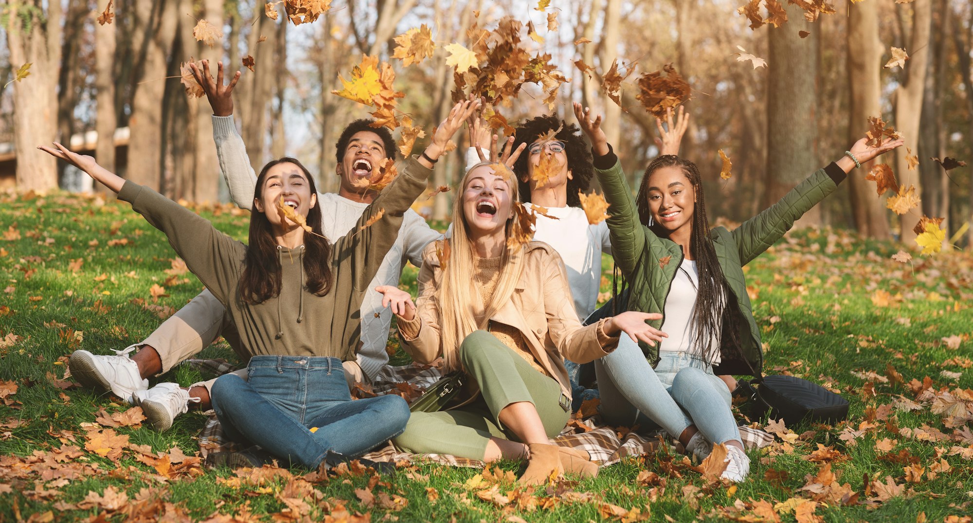 Happy students playing with golden leaves in park